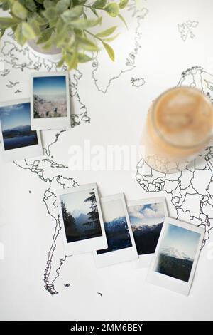 Polaroid-Fotos auf Travel World-Karte mit Eiskaffee und Pflanzen Stockfoto