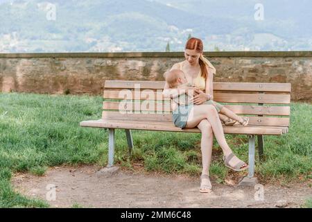 Eine weiße Frau, die ihr kleines Mädchen in einem Park stillt Stockfoto