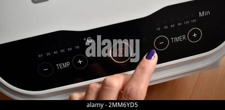 Weibliche Hand, die Temperatur und Zeit am Gerät steuert Stockfoto