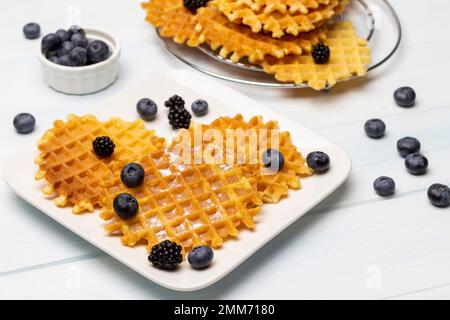 Wiener Waffeln und Beeren auf einem weißen Teller. Blaubeeren in einer Schüssel. Weißer Hintergrund. Stockfoto