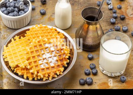 Wafer in Metallschüssel. Beeren in weißer Schüssel. Milch im Glas. Cezve und Blaubeeren auf dem Tisch. Draufsicht. Rostiger Hintergrund. Stockfoto