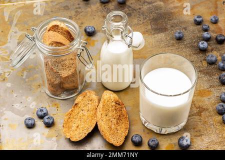 Cracker in einem Glasgefäß und auf dem Tisch. Milch in einem Glas und in einer Flasche. Heidelbeere. Draufsicht. Rostiger Hintergrund. Stockfoto