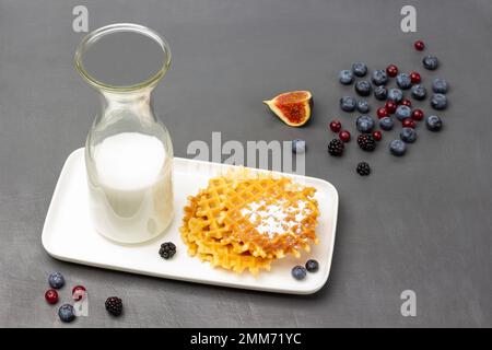 Waffeln und Milch in der Flasche auf weißem Teller. Feigen und Beeren auf dem Tisch. Draufsicht. Grauer Hintergrund. Stockfoto