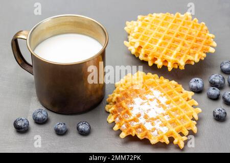 Waffeln und Beeren auf dem Tisch. Milch in einem Metallbecher. Draufsicht. Grauer Hintergrund. Stockfoto