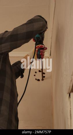 Lochungen in Form eines Kreises in der Wand unter der Decke im Raum mit einem Bohrer, Bohren der Wand, um Löcher für die Raumbelüftung zu bohren Stockfoto