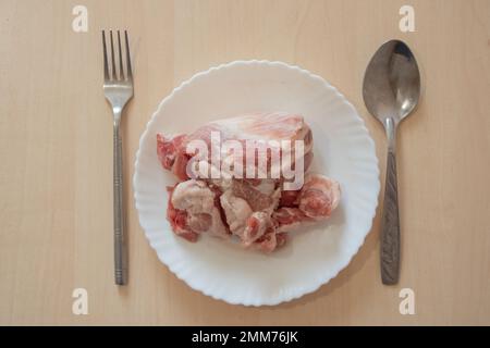 Ein Stück rohes Schweinefleisch liegt auf einem weißen Teller auf dem Tisch Stockfoto