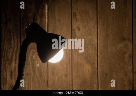 Die Tischleuchte leuchtet in einem dunklen Raum auf dem Tisch auf Stockfoto