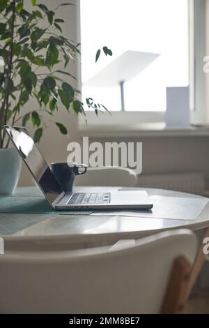 Laptop auf Tisch mit Tasse Kaffee im Heimbüro mit moderner Internet-Technologie, Arbeit von zu Hause aus Konzept. Stockfoto