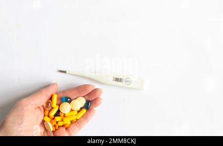 Elektronisches Thermometer und Pillen in der Hand auf weißem Hintergrund Stockfoto