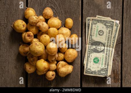 Eine junge rothaarige kleine geschälte Kartoffel liegt auf einem Holztisch in der Nähe und es sind Dollars daneben Stockfoto