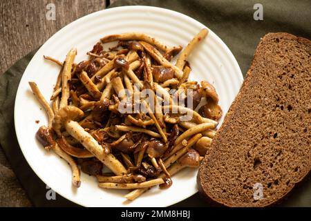 Gebratene Honigpilze auf einem Teller mit einem Stück Schwarzbrot auf einem alten Holztisch, gebratene Pilze zu Hause, Mittagessen Stockfoto