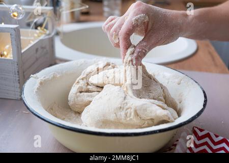 Hände kneten dicken Teig auf den Küchentisch, dekoriert mit festlichen Dekorationen zu Weihnachten und Neujahr. Backen zu Hause, Aroma und Komfort. Schließen- Stockfoto