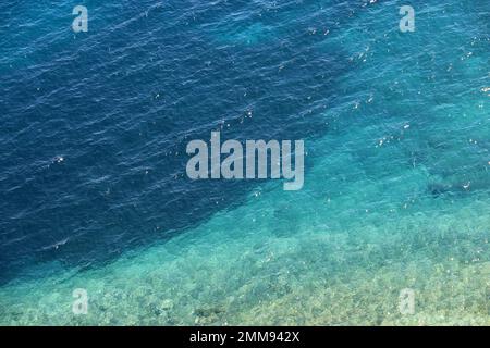 Azurblaue Wassertextur, transparente Meeresoberfläche mit felsigem Boden. Luftaufnahme, natürlicher türkisfarbener Hintergrund Stockfoto