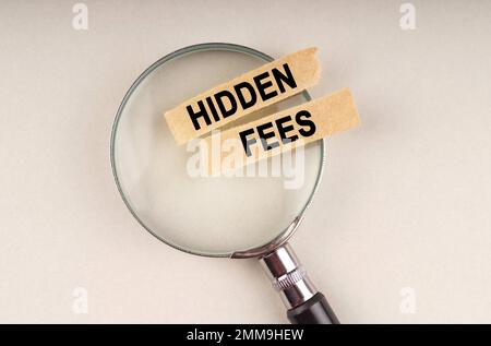 Auf der Lupe befinden sich Papierstreifen mit der Aufschrift "versteckte Gebühren". Stockfoto