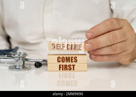 Medizinisches Konzept. Auf einer weißen Oberfläche stehen ein Stethoskop und Holzplatten mit der Aufschrift „Self Care“ an erster Stelle Stockfoto