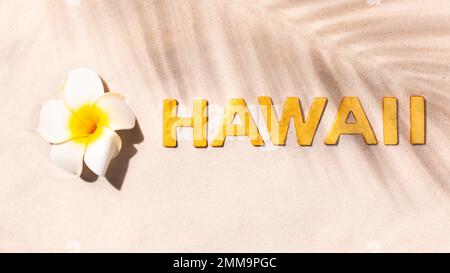 Hawaii - Plumeria-Blume und Inschrift mit goldenen Buchstaben auf weißem Sand Stockfoto