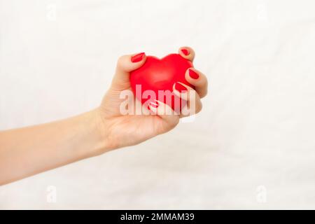 Frauenhand mit roter Maniküre, die rotes Herz auf weiß hält. Krankenschwestern pflegen Herz. Gute Gesundheitsförderung Stockfoto