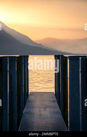 Ein Steg auf dem See während des Sonnenuntergangs in der Ferne fliegt eine Möwe Stockfoto