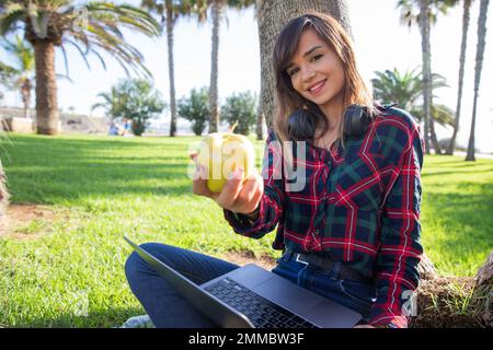 Ein attraktives Mädchen in einem öffentlichen Park mit einem gebissenen Apfel, gesunder Lebensstil Stockfoto