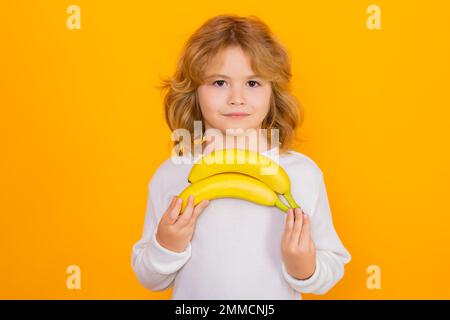 Vitamin und gesunde Früchte für Kinder. Kinderspiel-Banane im Studio. Studioporträt eines süßen Jungen mit Bananen isoliert auf Gelb. Stockfoto