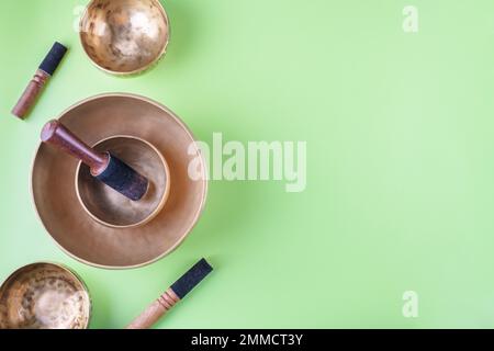 Tibetische Gesangsschüsseln mit Stöcken, die bei Mantra-Meditationen auf grünem Hintergrund, flach liegend, Webbanner verwendet werden Stockfoto