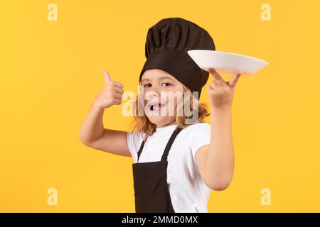 Lustiger Kinderkoch mit Kochplatte. Kid Chef Cook bereitet Speisen auf isoliertem Studiohintergrund zu. Kinder kochen. Teenager mit Schürze und Kochmütze Stockfoto