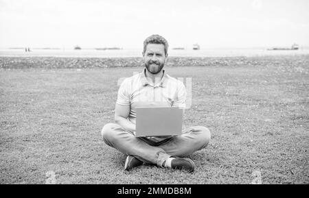 Glücklicher Geschäftsmann mit Laptop zum Bloggen auf grünem Gras, Freiberufler Stockfoto
