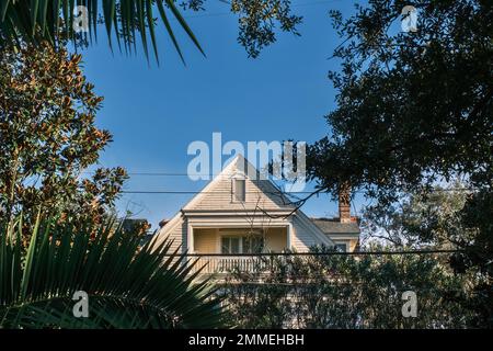 NEW ORLEANS, LA, USA - 27. JANUAR 2023: Versenkter Giebelbalkon im oberen Stockwerk eines historischen Wohnhauses aus der Kolonialzeit, eingerahmt von Baumzweigen Stockfoto