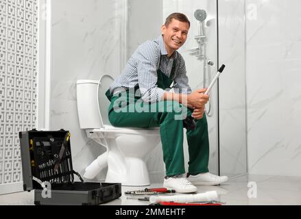 Professioneller Klempner mit Kolben, der auf der Toilettenschüssel im Badezimmer sitzt Stockfoto