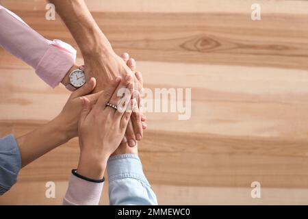 Personen, die ihre Hände über einem Holzhintergrund zusammenhalten, Draufsicht mit Platz für Text. Einheitskonzept Stockfoto