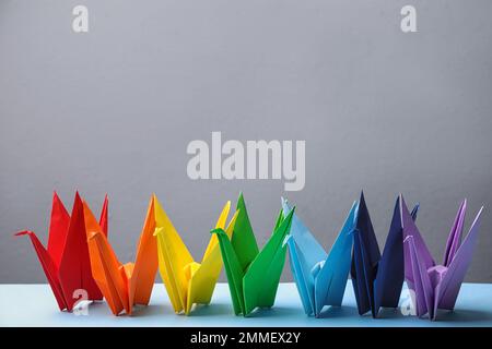 Bunte Origami-Figuren auf einem hellblauen Tisch. Regenbogenpalette Stockfoto