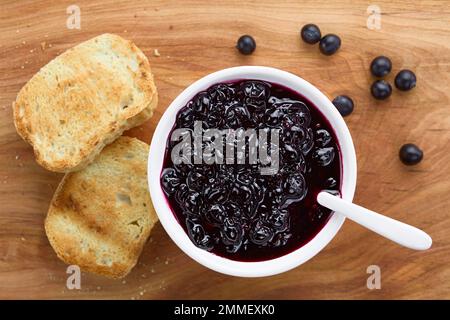 Frische hausgemachte Marmelade aus patagonischen Calafatbeeren (lat. Berberis heterophylla) serviert mit Löffel in weißer Schüssel, getoastetes Brot an der Seite Stockfoto