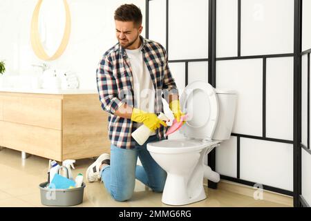 Junger Mann fühlt sich angewidert, als er die Toilettenschüssel im Bad reinigte Stockfoto