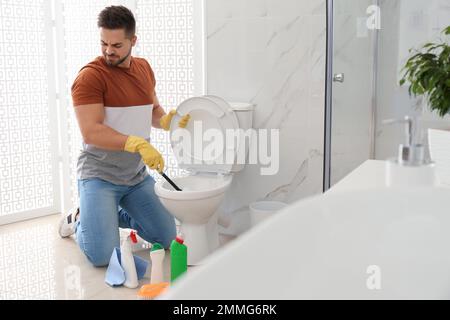 Junger Mann fühlt sich angewidert, als er die Toilettenschüssel im Bad reinigte Stockfoto