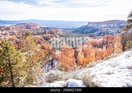 Der Bryce Canyon ist mit frisch gefallenem Schnee und fernen Bergen und leuchtend farbigen orangefarbenen Klippen geschmückt. Stockfoto