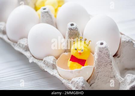 Ein kleines Huhn in einer zerbrochenen Schale in der Nähe von weißen Hühnereiern. Ostern ist das Konzept der Einsamkeit. Ostereier in Eierkarton Stockfoto