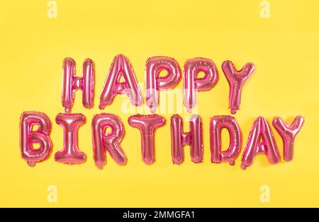 Satz HAPPY BIRTHDAY (ALLES GUTE ZUM GEBURTSTAG) aus pinkfarbenen Buchstaben aus Folienballon auf gelbem Hintergrund Stockfoto