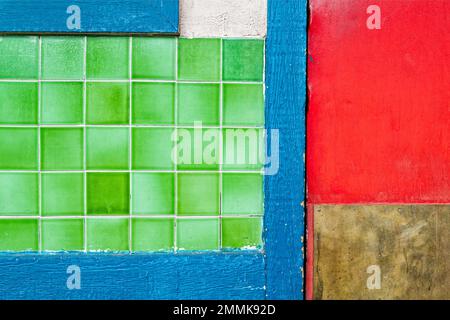 Grüne Fliesen in blauem Holzrahmen mit roter Tür an einer Außenwand Stockfoto