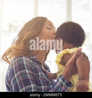 Sie schenkt ihrem Baby die Liebe, die sie braucht. Eine junge Mutter und ihr kleines Mädchen zu Hause. Stockfoto