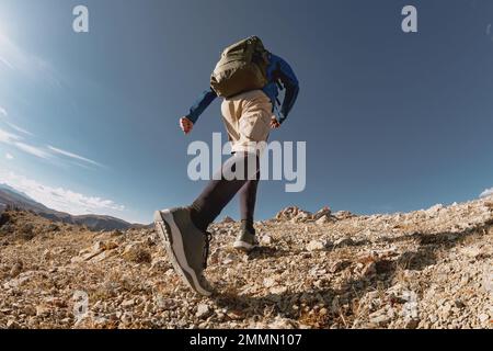 Sportlicher Mann mit Rucksack bergauf in den Bergen. Nahaufnahme von unten Stockfoto