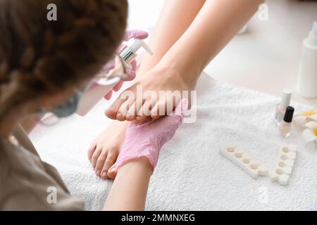 Kosmetikerin, die Creme auf das Bein einer Frau aufträgt, im Salon, Nahaufnahme Stockfoto