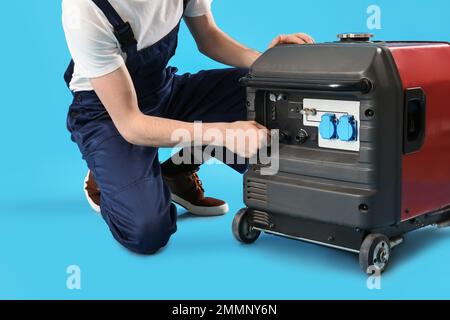 Männlicher Arbeiter mit tragbarem Benzingenerator auf blauem Hintergrund Stockfoto