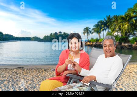 Glückliches älteres Paar, das auf einem Liegestuhl sitzt, trinkt Champagner Stockfoto