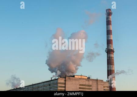 Ziegelschornstein mit weißem Rauch über einem Industriegebäude. Stockfoto