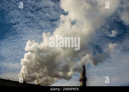 Weißer und grauer Rauch und Dampf aus einem hohen Betonkamin am hellblauen Himmel. Stockfoto