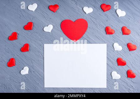 Liebesbrief, valentinskarte für Angehörige. Leeres weißes Blatt Papier, umgeben von weißen und roten Herzformen auf grauem Trendhintergrund, Kopie Spak Stockfoto