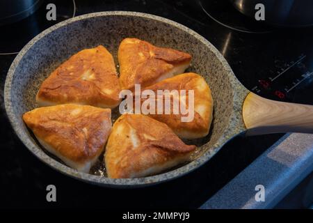 Zubereitung von Belyashes auf einer Bratpfanne. Traditionelle russische Fleischpasteten belyashi. Russische Küche. Stockfoto