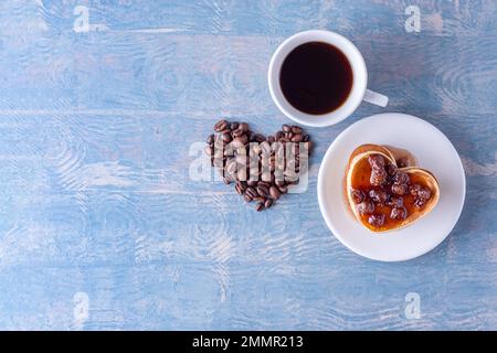 Frühstück für deine Geliebte. Hausgemachte herzförmige Pfannkuchen mit Beerenmarmelade, herzförmig aus Kaffeebohnen und einer weißen Tasse heißem Kaffee auf einem blauen Stockfoto