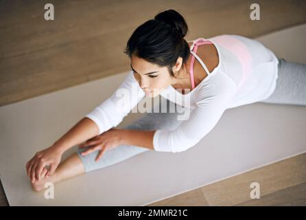 Ihr Wohlbefinden mit Yoga in Schach zu halten. Eine junge Frau, die sich während ihrer Yoga-Routine dehnt. Stockfoto