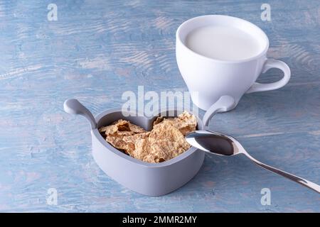 Gesundes Frühstück für Kinder. Haferflocken in einer herzförmigen Schüssel, ein Löffel und eine weiße Tasse Milch auf einem blauen Holztisch, Kopierbereich. Gesundes Essen conce Stockfoto